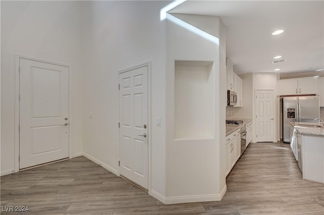 kitchen with sink, light stone countertops, light hardwood / wood-style floors, white cabinetry, and stainless steel appliances