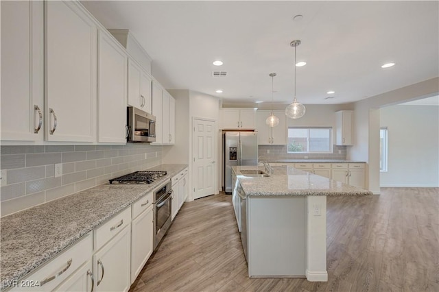 kitchen featuring hanging light fixtures, stainless steel appliances, light hardwood / wood-style flooring, a center island with sink, and white cabinets