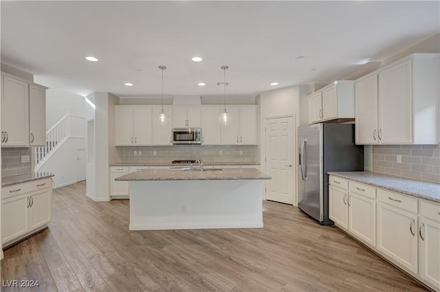 kitchen featuring light stone countertops, hanging light fixtures, light hardwood / wood-style floors, a kitchen island with sink, and appliances with stainless steel finishes