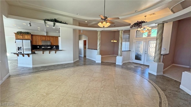 interior space featuring french doors, decorative columns, ceiling fan with notable chandelier, a tray ceiling, and light tile patterned floors