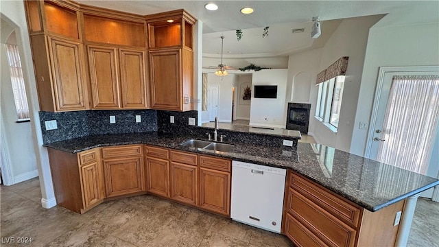 kitchen with dishwasher, sink, ceiling fan, dark stone countertops, and tasteful backsplash