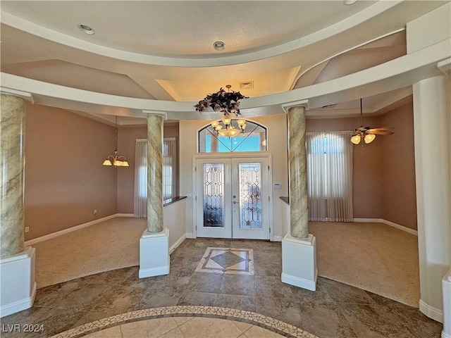 foyer entrance with french doors, ceiling fan with notable chandelier, decorative columns, and carpet floors