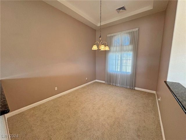 empty room with a raised ceiling, carpet floors, and an inviting chandelier