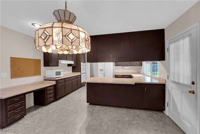 kitchen featuring under cabinet range hood, dark brown cabinets, white appliances, and light countertops