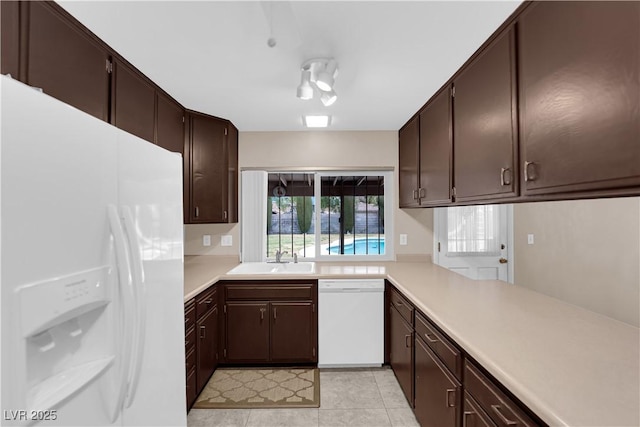 kitchen with a sink, white appliances, dark brown cabinetry, light countertops, and light tile patterned floors