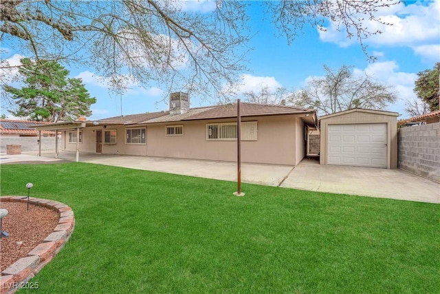 back of house with stucco siding, an outbuilding, a lawn, fence, and concrete driveway