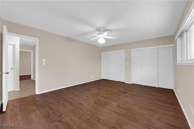 unfurnished bedroom featuring baseboards, multiple closets, dark wood-type flooring, and a ceiling fan