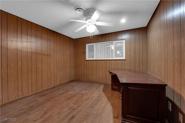 unfurnished office featuring ceiling fan, a textured ceiling, wood finished floors, and wood walls