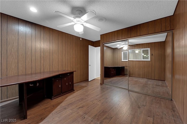 unfurnished bedroom with a ceiling fan, wood finished floors, a closet, wood walls, and a textured ceiling