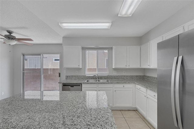 kitchen with light tile patterned flooring, sink, white cabinets, light stone counters, and stainless steel appliances