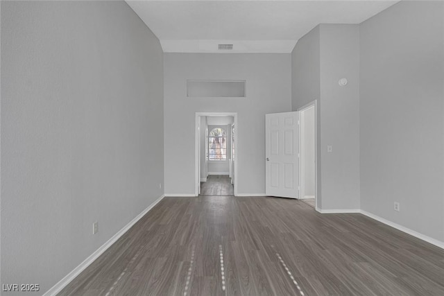 empty room featuring a towering ceiling and dark wood-type flooring