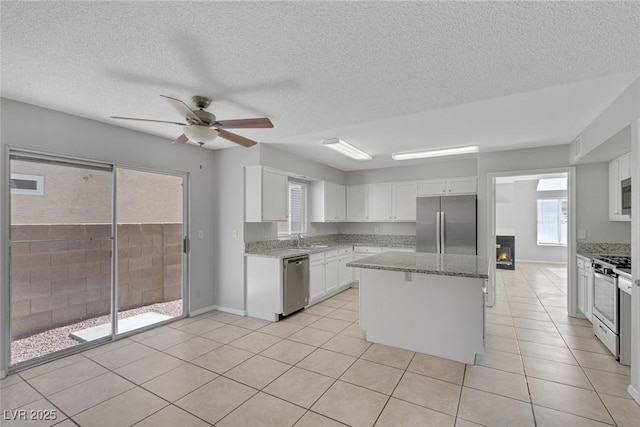 kitchen with sink, appliances with stainless steel finishes, a center island, light stone countertops, and white cabinets