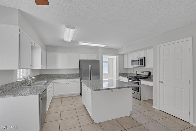 kitchen featuring sink, light tile patterned floors, stainless steel appliances, white cabinets, and a kitchen island