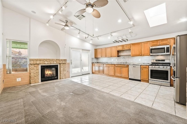 kitchen with a skylight, ceiling fan, stainless steel appliances, a fireplace, and light tile patterned flooring