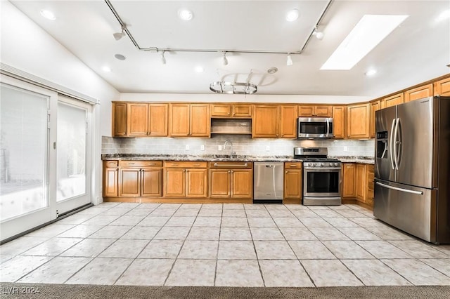 kitchen featuring appliances with stainless steel finishes, backsplash, a skylight, and light stone counters