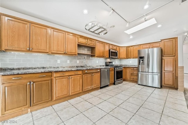 kitchen with lofted ceiling with skylight, sink, light tile patterned floors, appliances with stainless steel finishes, and light stone counters