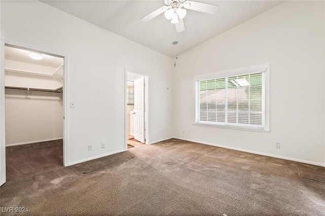 unfurnished bedroom with connected bathroom, ceiling fan, lofted ceiling, a walk in closet, and dark carpet