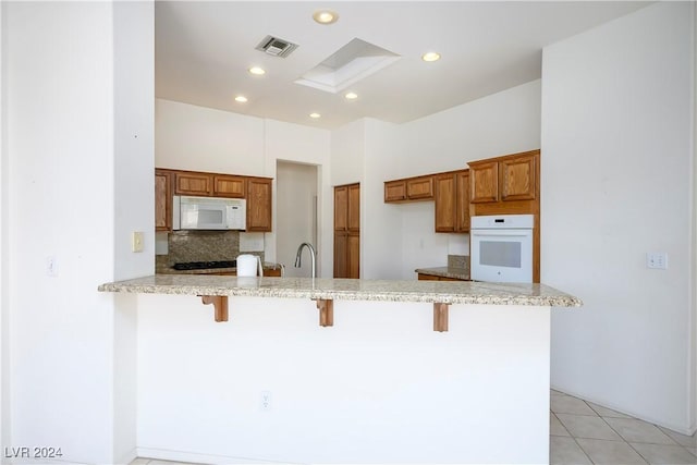 kitchen with tasteful backsplash, kitchen peninsula, white appliances, a kitchen bar, and light tile patterned floors