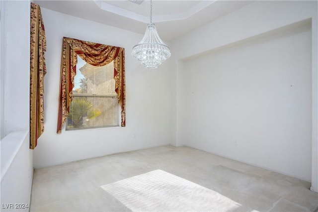 spare room with carpet floors, a tray ceiling, and an inviting chandelier