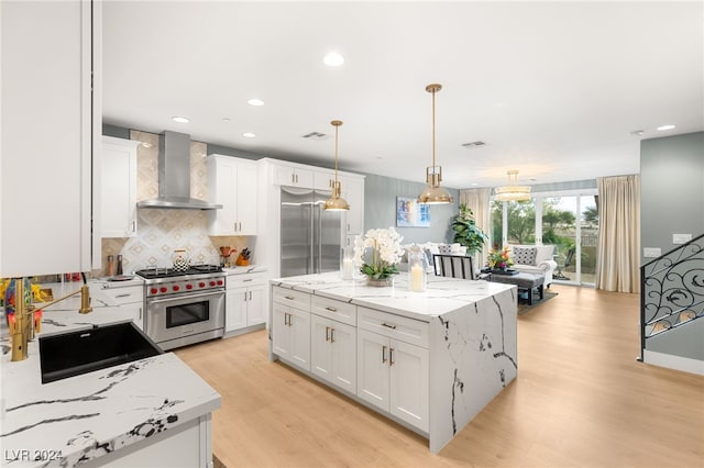 kitchen with high quality appliances, a center island, white cabinetry, and wall chimney exhaust hood