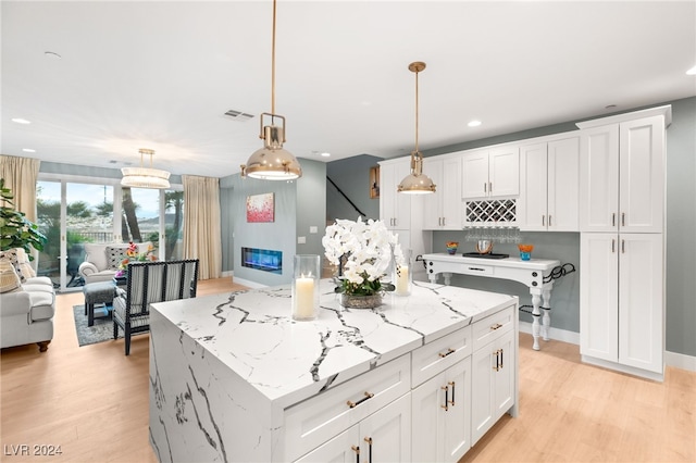 kitchen featuring white cabinets, a kitchen island, decorative light fixtures, and light wood-type flooring