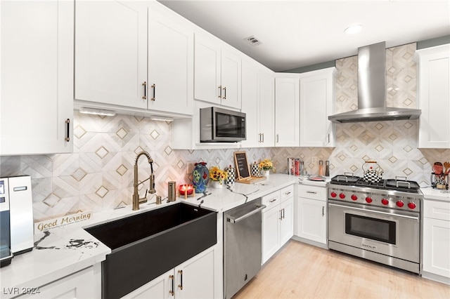 kitchen featuring sink, wall chimney exhaust hood, decorative backsplash, appliances with stainless steel finishes, and white cabinetry