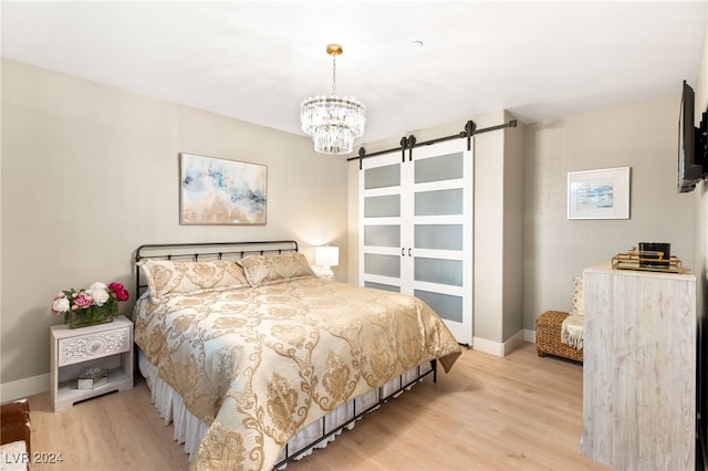 bedroom featuring a barn door, light hardwood / wood-style floors, and an inviting chandelier