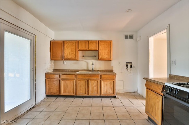 kitchen featuring light tile patterned flooring, black gas range oven, and sink