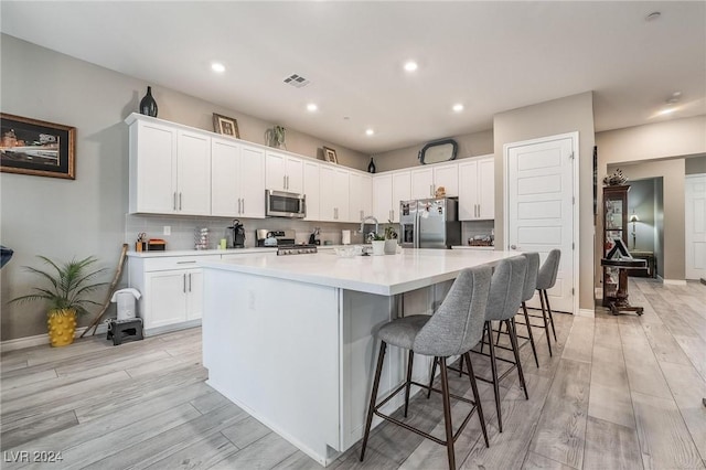 kitchen with white cabinetry, a center island with sink, light wood-type flooring, and appliances with stainless steel finishes