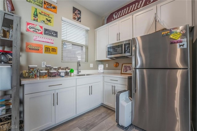 kitchen with sink, white cabinetry, stainless steel appliances, and light hardwood / wood-style flooring