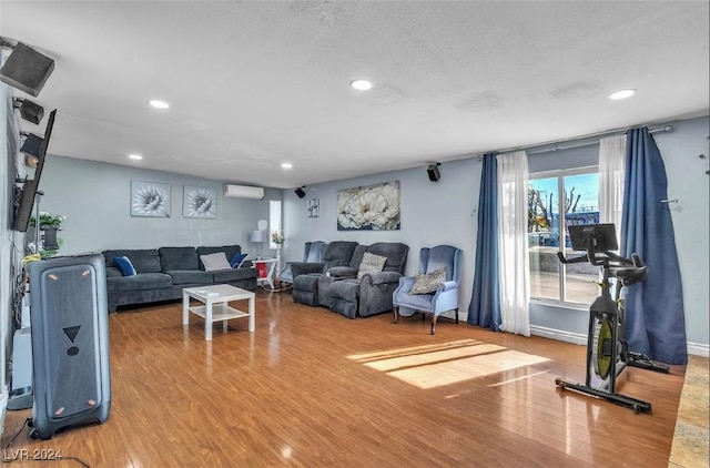 living room featuring wood-type flooring, a textured ceiling, and an AC wall unit