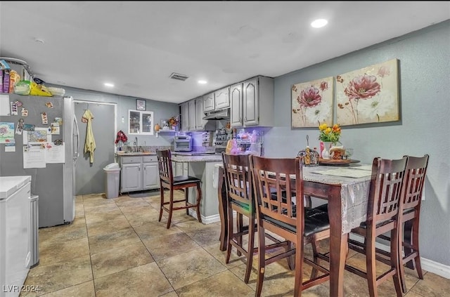 interior space with stainless steel refrigerator, gray cabinetry, sink, and a kitchen breakfast bar