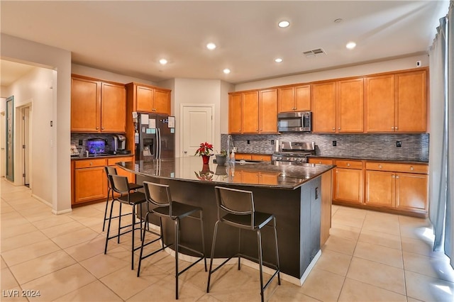 kitchen featuring a breakfast bar area, a large island with sink, tasteful backsplash, and appliances with stainless steel finishes