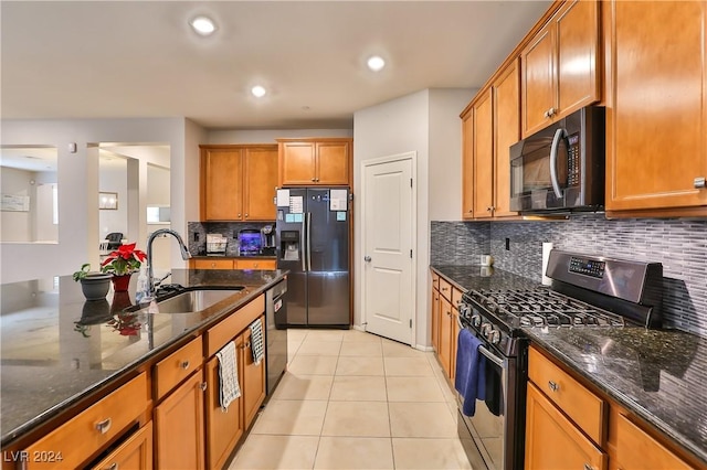 kitchen with decorative backsplash, dark stone counters, stainless steel appliances, sink, and light tile patterned floors