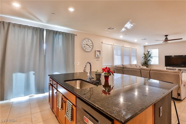 kitchen with sink, stainless steel dishwasher, an island with sink, dark stone counters, and light tile patterned floors