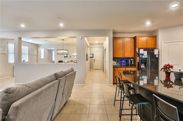 kitchen featuring pendant lighting, an inviting chandelier, light tile patterned flooring, black fridge with ice dispenser, and a breakfast bar area