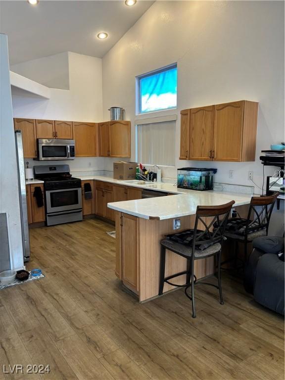 kitchen with light hardwood / wood-style floors, kitchen peninsula, appliances with stainless steel finishes, a breakfast bar area, and high vaulted ceiling