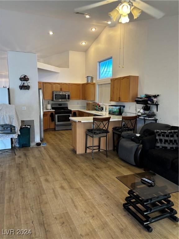 kitchen featuring kitchen peninsula, appliances with stainless steel finishes, high vaulted ceiling, light hardwood / wood-style flooring, and a breakfast bar