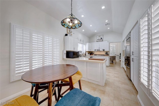 kitchen featuring white cabinetry, kitchen peninsula, pendant lighting, vaulted ceiling, and light tile patterned floors