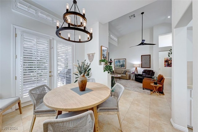 tiled dining room with a towering ceiling and ceiling fan with notable chandelier