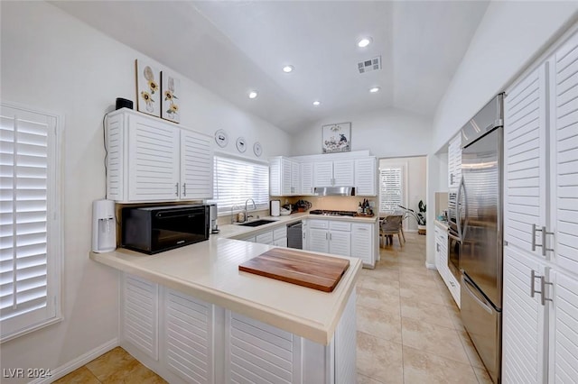 kitchen featuring kitchen peninsula, stainless steel appliances, vaulted ceiling, sink, and white cabinets