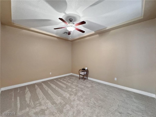 empty room featuring ceiling fan, a raised ceiling, light colored carpet, and a textured ceiling