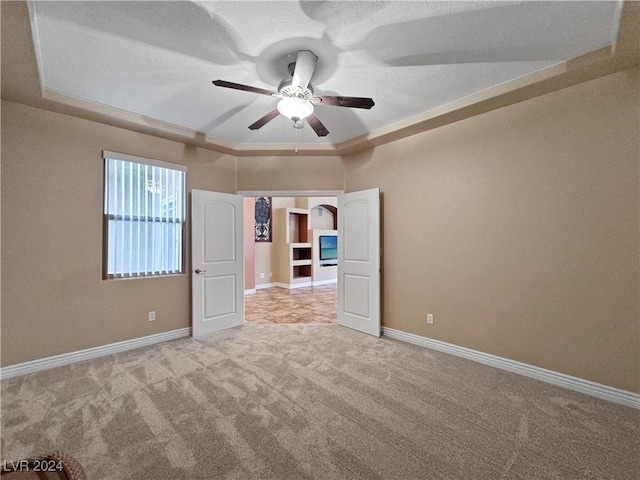 spare room with carpet flooring, crown molding, a tray ceiling, and ceiling fan