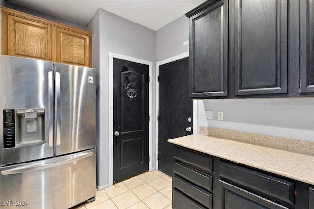 kitchen with stainless steel fridge, light stone countertops, and light tile patterned floors