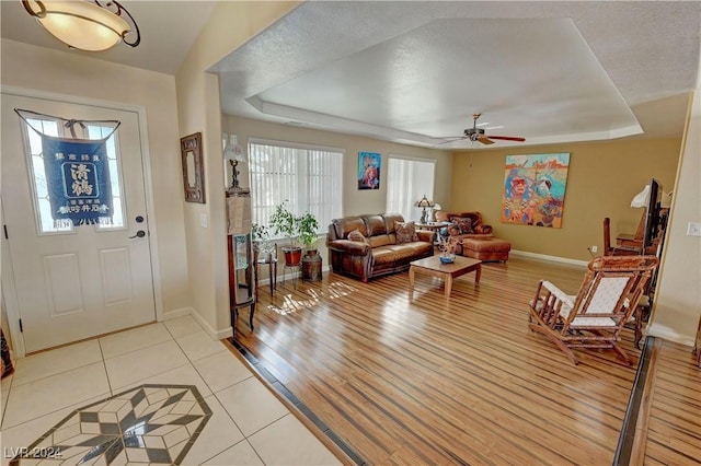 tiled entrance foyer with a textured ceiling, a tray ceiling, and ceiling fan