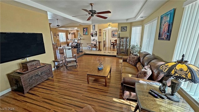 living room featuring wood-type flooring, a tray ceiling, and ceiling fan