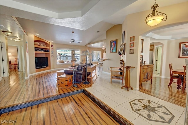 living room featuring ceiling fan, built in features, light tile patterned floors, and vaulted ceiling