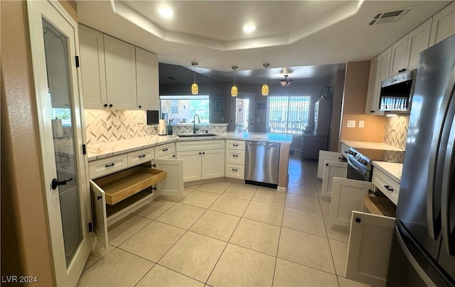 kitchen featuring appliances with stainless steel finishes, a raised ceiling, sink, decorative light fixtures, and white cabinetry