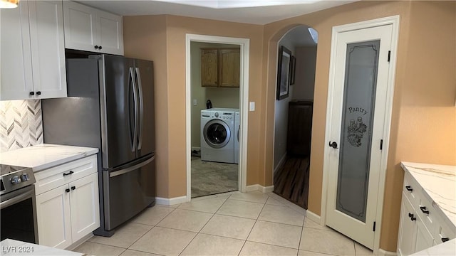 kitchen featuring tasteful backsplash, light stone counters, washer / clothes dryer, white cabinetry, and light tile patterned flooring