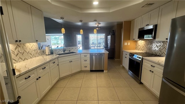 kitchen featuring pendant lighting, sink, appliances with stainless steel finishes, a tray ceiling, and white cabinetry